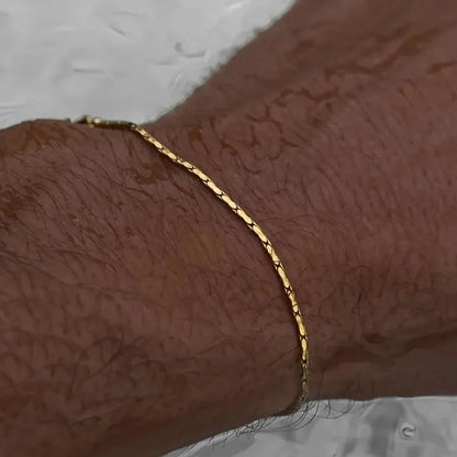Gold wire chain bracelet worn on a wet wrist, with a reflective wet surface in the background.