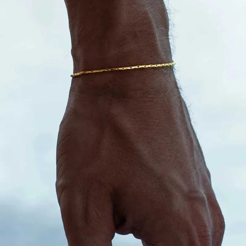 Gold wire chain bracelet worn on the wrist, outdoors against a cloudy sky background.