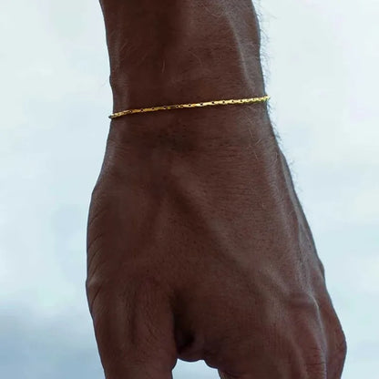 Gold wire chain bracelet worn on the wrist, outdoors against a cloudy sky background.