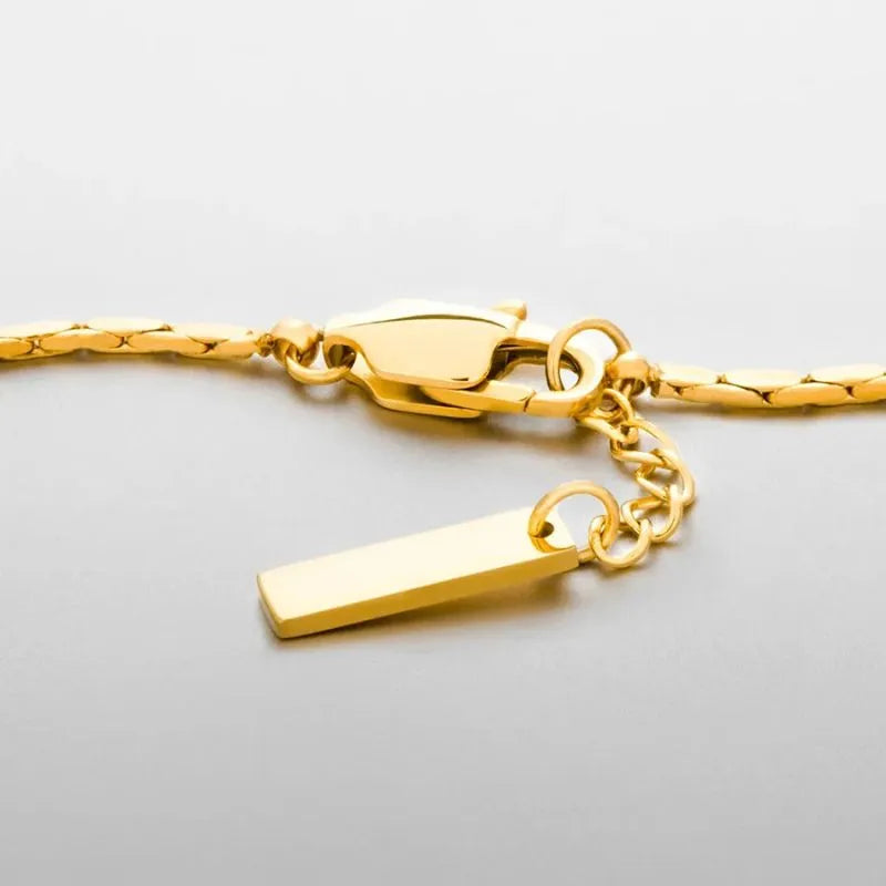 Close-up of the gold wire bracelet's clasp, bar tag charm, and extension chain on a light grey background.