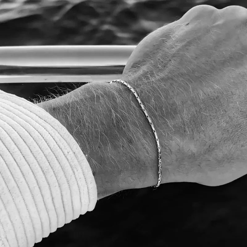 Black-and-white photo of the wire bracelet worn on the wrist, resting against a boat railing with the ocean in the background.