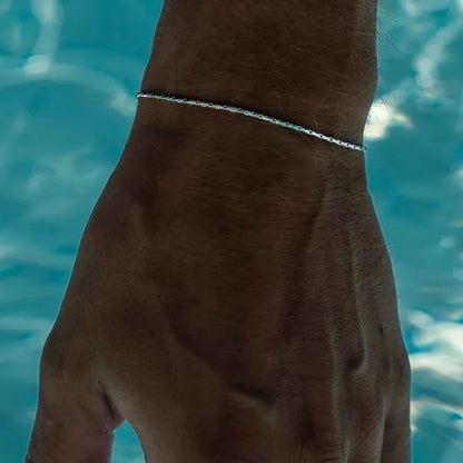 Silver-tone wire chain bracelet worn on the wrist poolside, with turquoise pool water in the background.