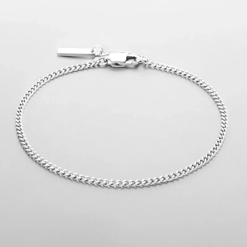 Thin silver Cuban curb chain bracelet with a small rectangular bar tag charm, on a plain white background