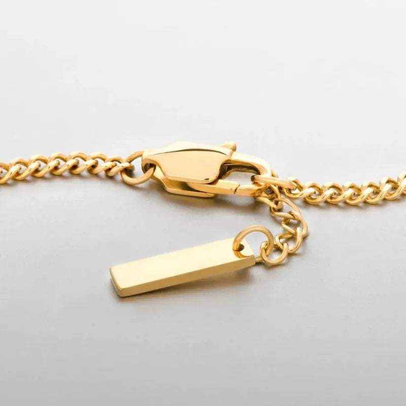 Close-up of the gold curb chain bracelet's lobster clasp and rectangular bar tag charm