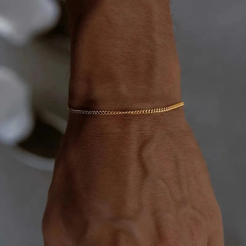 Wrist wearing the thin gold curb chain bracelet, natural daylight with a blurred grey background