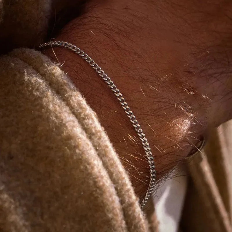 Close-up of a sunlit wrist wearing the thin silver curb chain bracelet, wearing a beige knit sweater