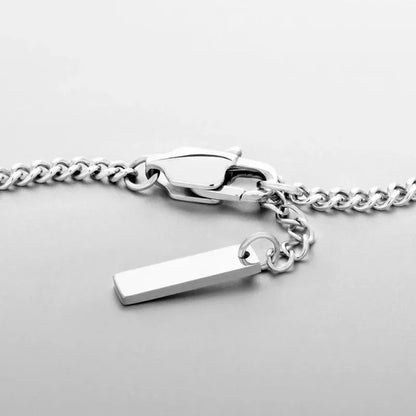 Close-up of the silver curb chain bracelet's lobster clasp and rectangular bar tag charm