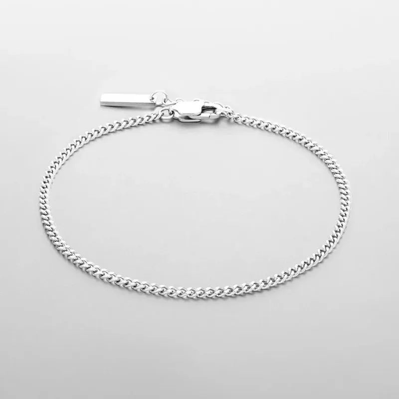 Thin silver Cuban curb chain bracelet with a rectangular bar tag charm, laid flat on a white background