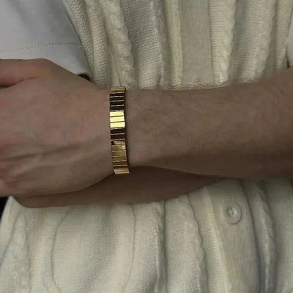 Wrist wearing the gold stretch bracelet with arms crossed, person in a cream cable-knit cardigan