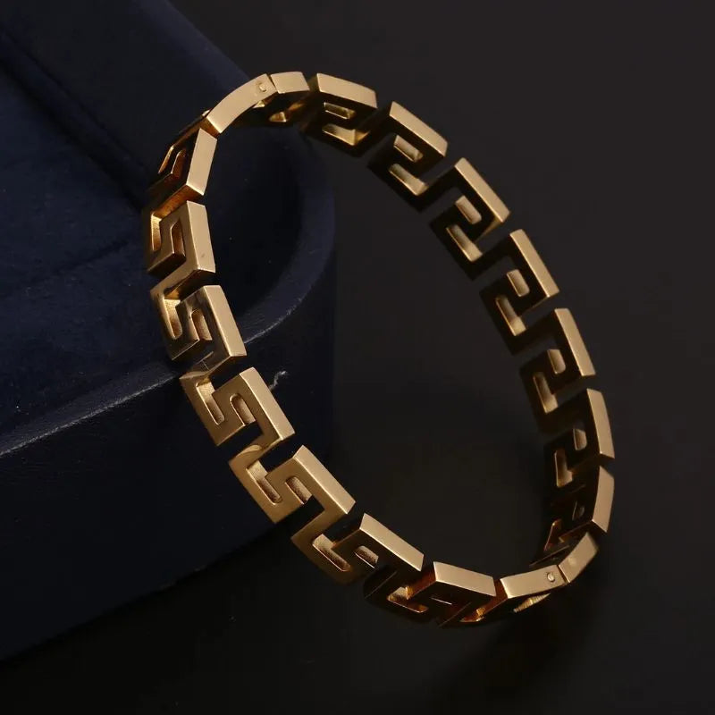 Gold Greek key bangle bracelet leaning against a navy blue jewellery box, photographed on a black background