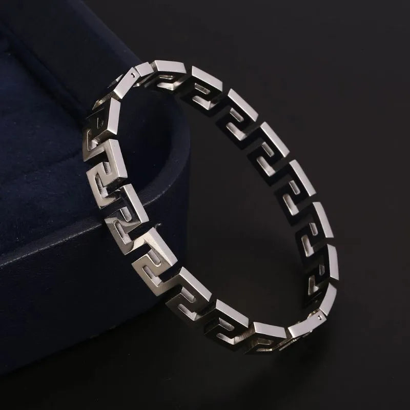 Silver Greek key bangle bracelet leaning against a navy blue jewellery box, photographed on a black background