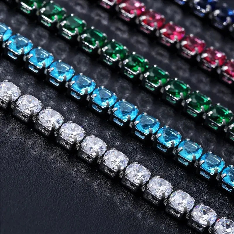Close-up of five tennis bracelets in different coloured stones showing the prong settings in detail on a textured black surface