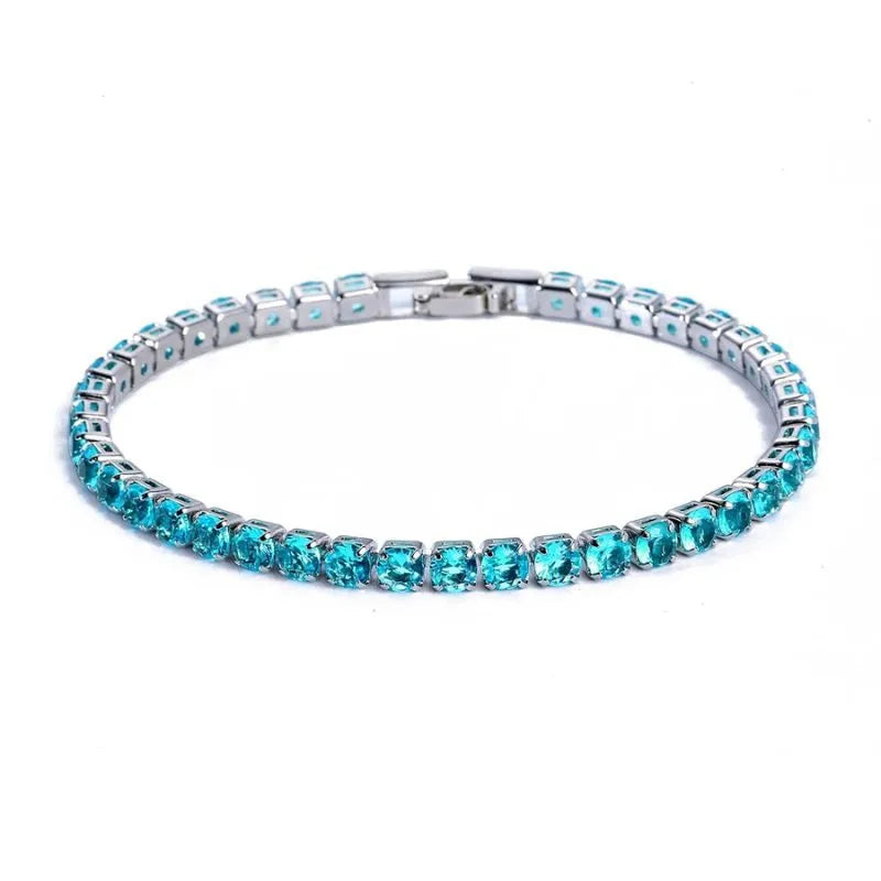 Tennis bracelet with turquoise-coloured stones in a silver setting, on a plain white background