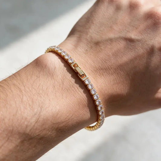Gold tennis bracelet with clear cubic zirconia stones, worn on a man's wrist.