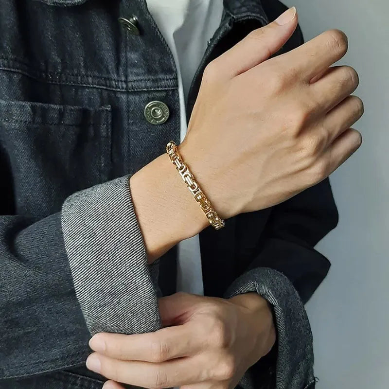 Gold Byzantine box-chain bracelet worn on the wrist, paired with a denim jacket outfit.
