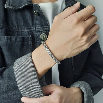Silver-tone Byzantine box-chain bracelet worn on the wrist, paired with a denim jacket outfit.
