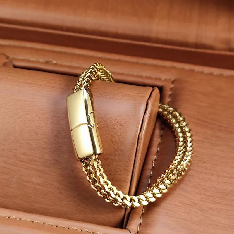 Close-up of the gold wheat chain bracelet's magnetic clasp, displayed on a tan leather jewellery cushion