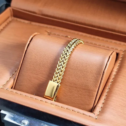 Overhead view of the gold wheat chain bracelet displayed upright inside an open tan leather jewellery box