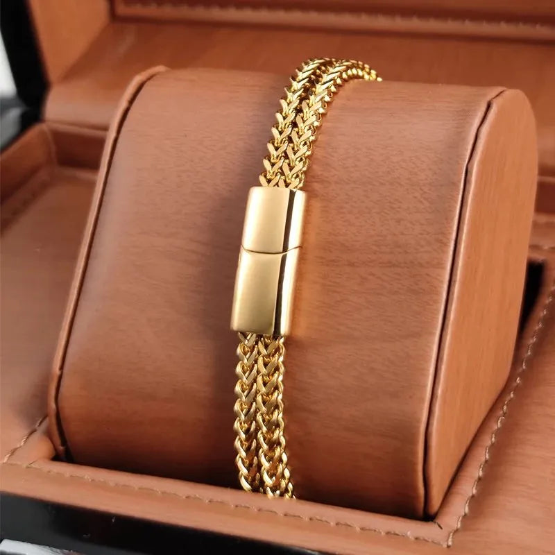 Gold wheat link chain bracelet with a magnetic push clasp, displayed on a tan leather jewellery stand