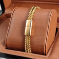 Gold wheat link chain bracelet with a magnetic push clasp, displayed on a tan leather jewellery stand