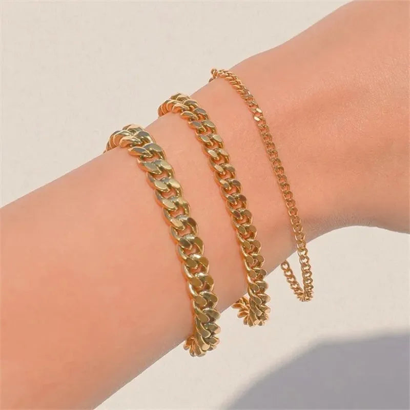 Three gold Cuban chain bracelets of different widths stacked on the wrist in bright natural light.