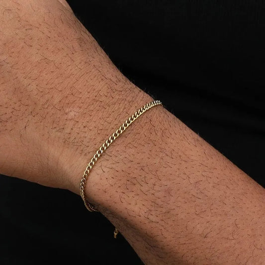 Thin gold Cuban chain bracelet worn on the wrist, close-up against a black background.