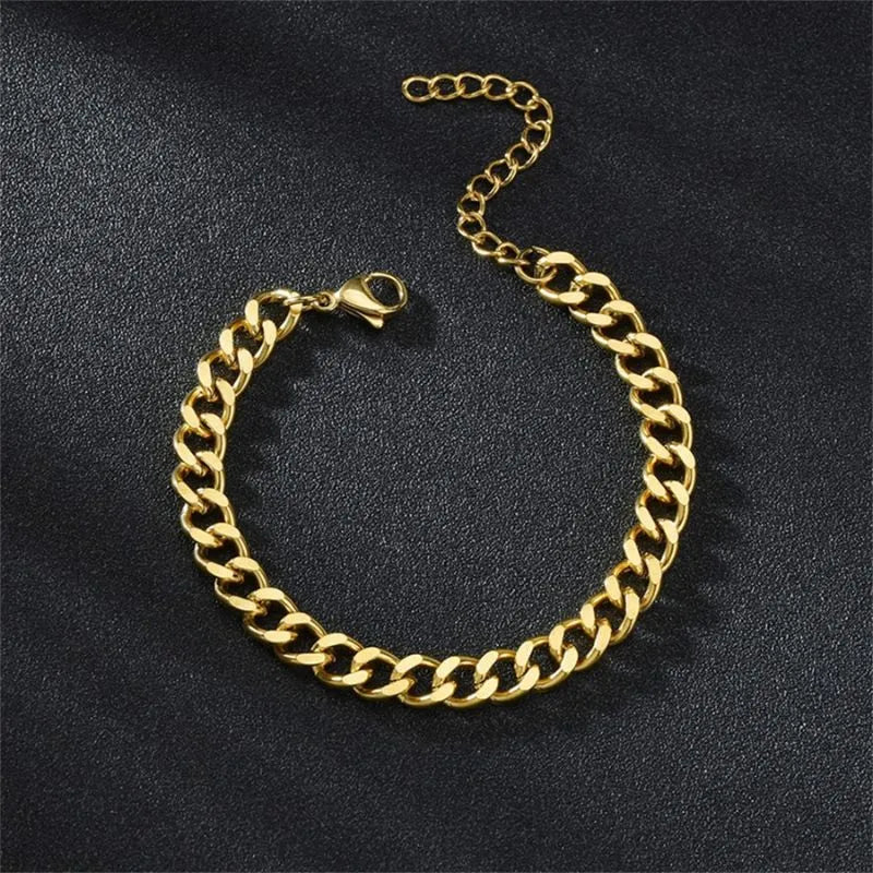 Gold Cuban chain bracelet laid flat in an oval shape on a black textured surface, with the lobster clasp and extension chain visible.