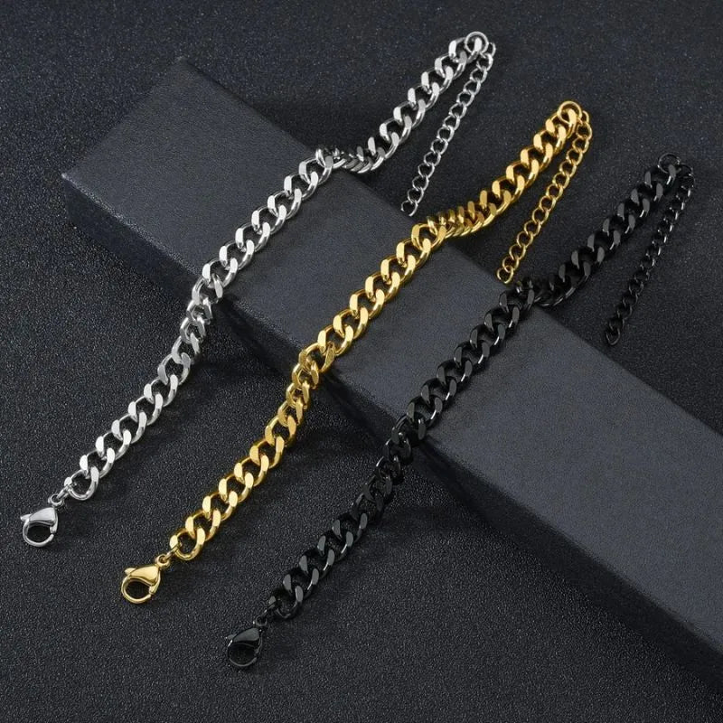 Silver, gold, and black-finish Cuban chain bracelets laid diagonally side by side on an angled black surface, comparing the available color options.