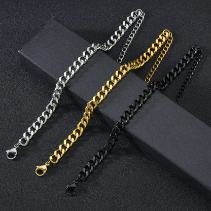 Silver, gold, and black-finish Cuban chain bracelets laid diagonally side by side on an angled black surface, comparing the available color options.