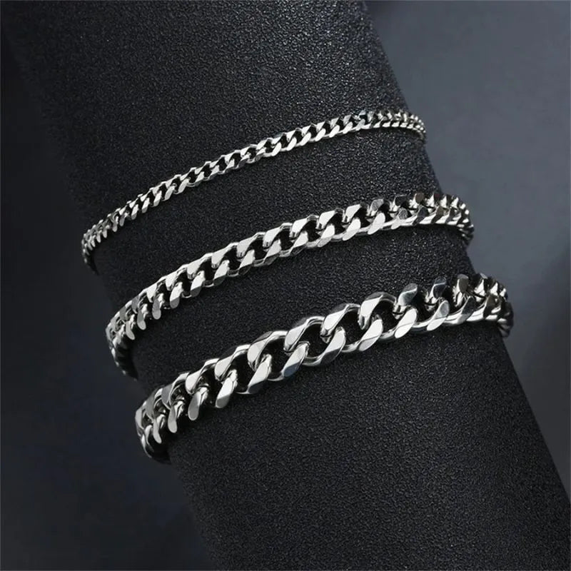 Three silver-tone Cuban chain bracelets of increasing width draped around a black display cylinder, showing the range of available widths.