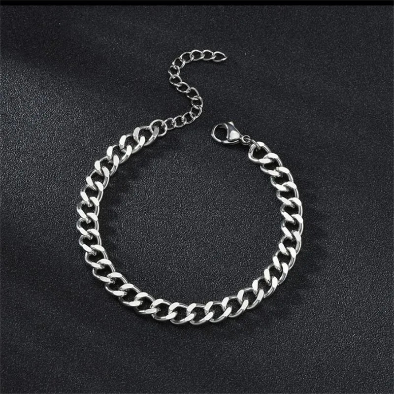 Silver-tone Cuban chain bracelet laid flat in an oval shape on a black textured surface, with the lobster clasp and extension chain visible.