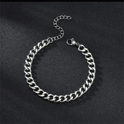 Silver-tone Cuban chain bracelet laid flat in an oval shape on a black textured surface, with the lobster clasp and extension chain visible.