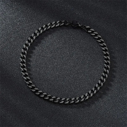 Black-finish Cuban chain bracelet laid flat in a circle on a black textured surface, with the lobster clasp and extension chain visible.
