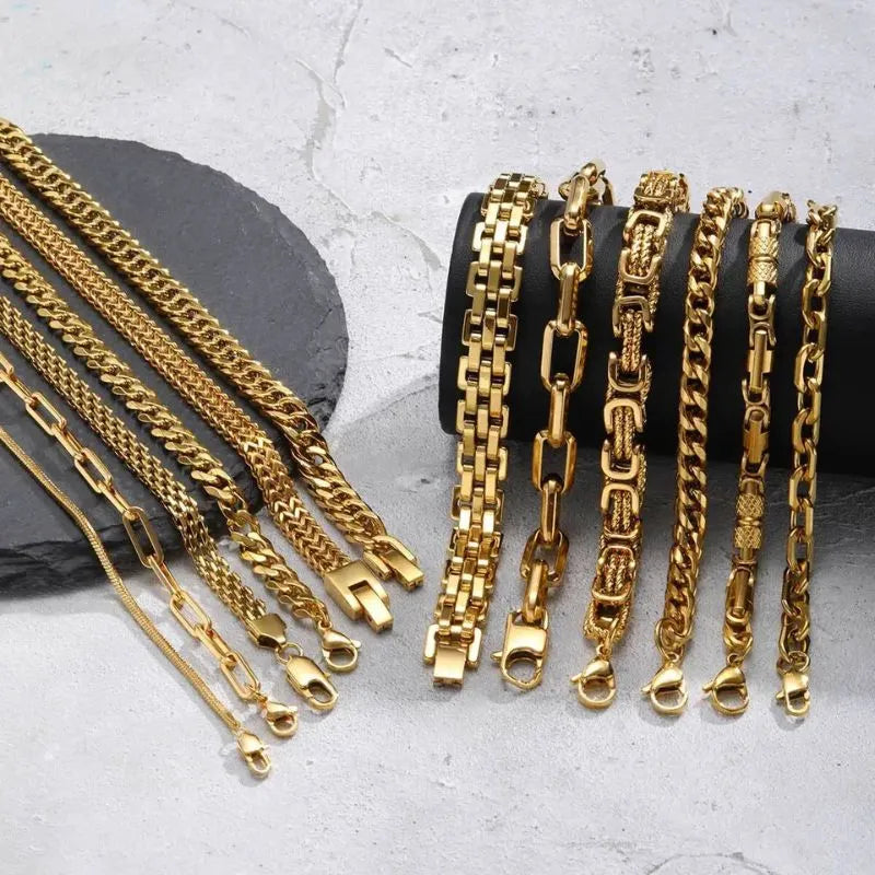 Wide view of around a dozen gold chain bracelet styles hanging over a black display stand on a marble surface