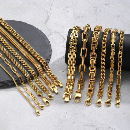 Wide view of around a dozen gold chain bracelet styles hanging over a black display stand on a marble surface