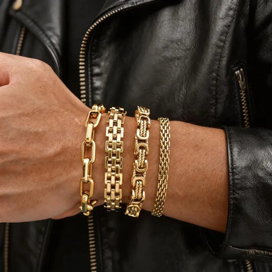 Four different gold chain bracelet styles stacked on a wrist, person wearing a black leather jacket