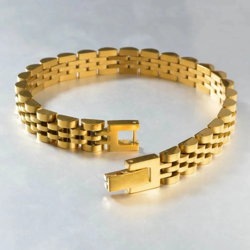 Gold jubilee-style watch link bracelet laid open on a light grey textured surface, showing the fold-over clasp unfastened