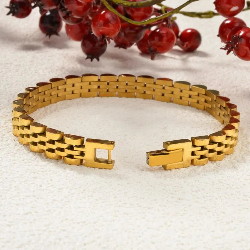 Gold watch link bracelet laid open on a white textured surface with red winter berries in the background