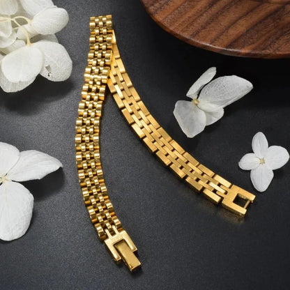 Gold watch link bracelet laid open diagonally on a black surface with white flowers and a wooden bowl edge