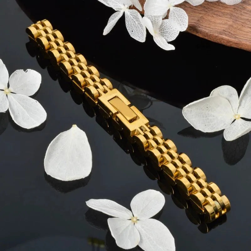 Gold watch link bracelet laid flat with clasp closed on a black surface surrounded by white flower petals