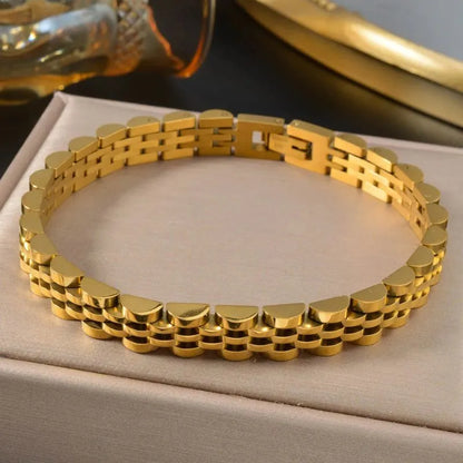 Gold watch link bracelet resting on a beige box with a blurred amber perfume bottle in the background