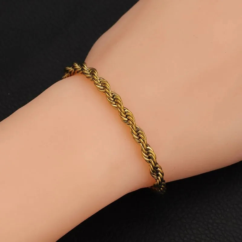 Gold twisted rope chain bracelet worn on the wrist against a black textured background.