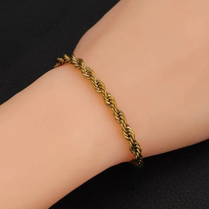 Gold twisted rope chain bracelet worn on the wrist against a black textured background.