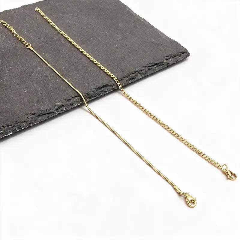 Two gold chains, a snake chain and a Cuban-style chain, laid flat on a plain white background.