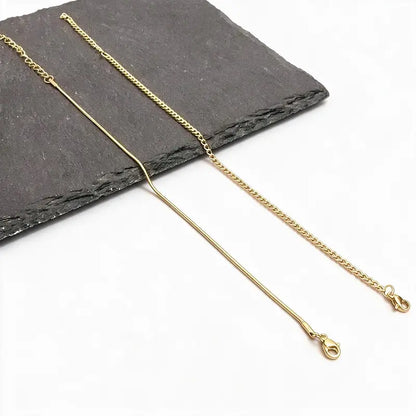 Two gold chains, a snake chain and a Cuban-style chain, laid flat on a plain white background.