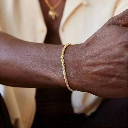 Gold twisted rope chain bracelet worn on the wrist, close-up on a man in a cream shirt with a gold necklace visible.