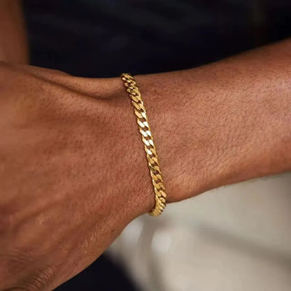 Close-up of a gold Cuban link bracelet resting on the wrist against a dark, blurred background.