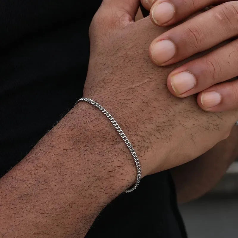 Silver-tone Cuban link bracelet worn on the wrist, with the other hand's fingers resting gently on top against a black background.