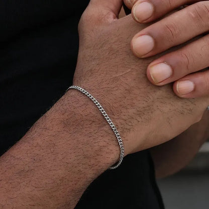 Silver-tone Cuban link bracelet worn on the wrist, with the other hand's fingers resting gently on top against a black background.