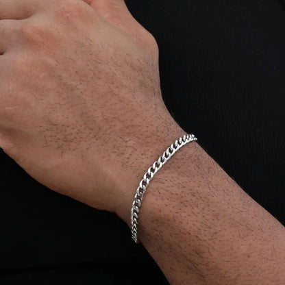 Silver-tone Cuban link bracelet worn on a closed fist, shown close-up against a black background.